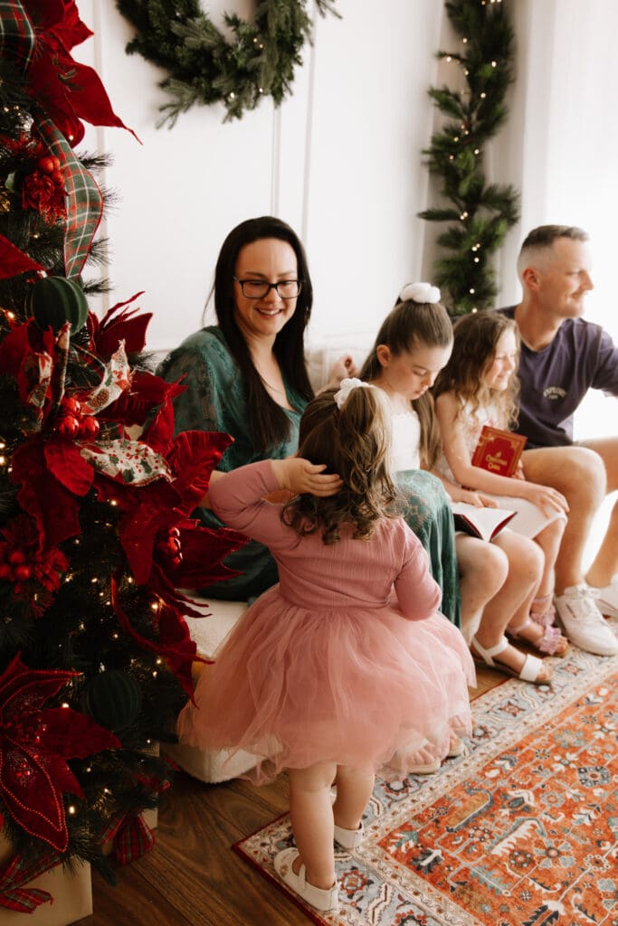 Family gathered on a cozy cream sofa with Christmas tree and wreath decorations during Sweet Moments Photography Christmas Minis in Wattle Grove.