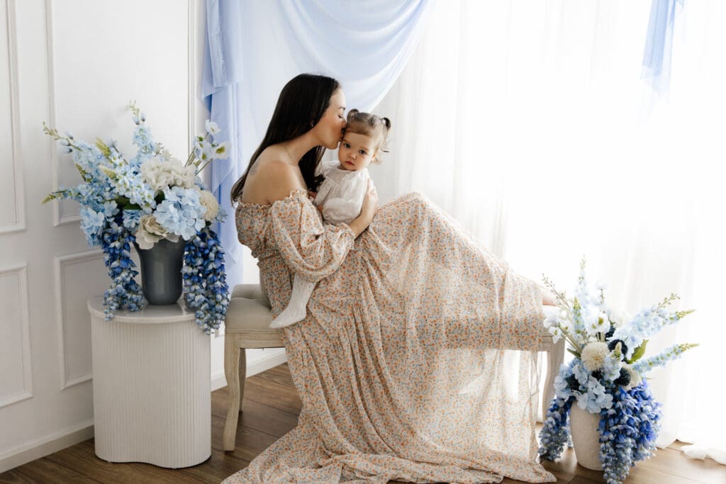 Mother kissing her baby on a bench surrounded by blue flowers during a Sydney Mother’s Day mini session