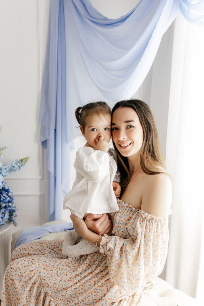 Mother and baby smiling at camera during Mother’s Day minis Sydney portrait session with soft blue backdrop